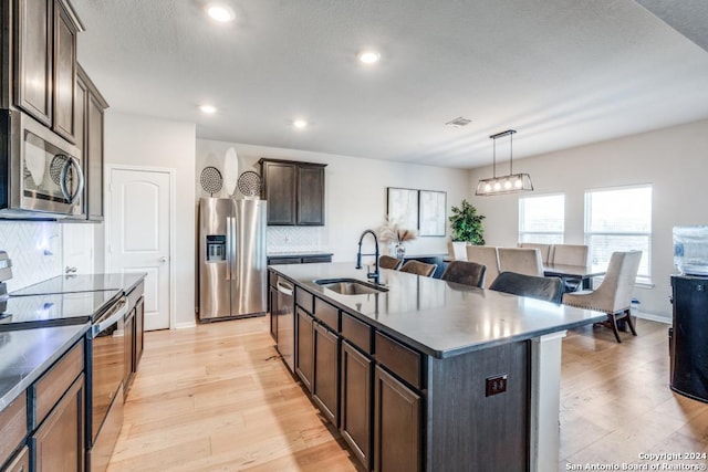 kitchen with sink, appliances with stainless steel finishes, a kitchen island with sink, dark brown cabinetry, and light wood-type flooring