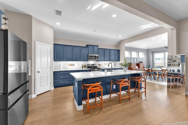 kitchen featuring a breakfast bar, blue cabinets, a kitchen island with sink, stainless steel appliances, and light wood-type flooring