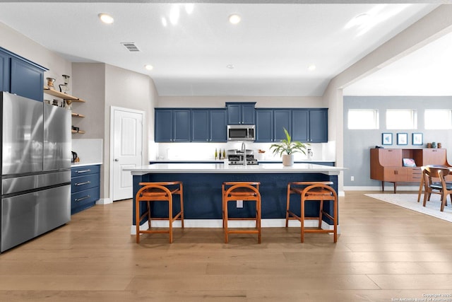 kitchen with appliances with stainless steel finishes, blue cabinets, and an island with sink