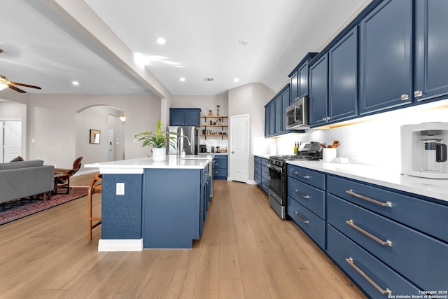 kitchen featuring blue cabinets, a breakfast bar area, a center island with sink, appliances with stainless steel finishes, and light hardwood / wood-style floors