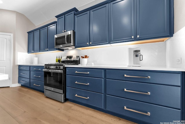 kitchen featuring blue cabinetry, lofted ceiling, appliances with stainless steel finishes, light hardwood / wood-style floors, and backsplash