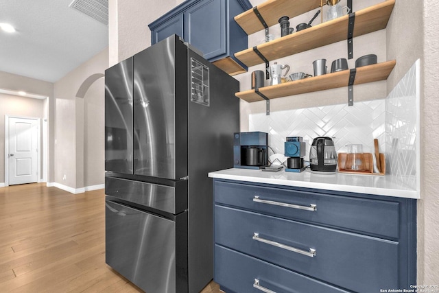 kitchen with stainless steel refrigerator, hardwood / wood-style flooring, blue cabinetry, and backsplash