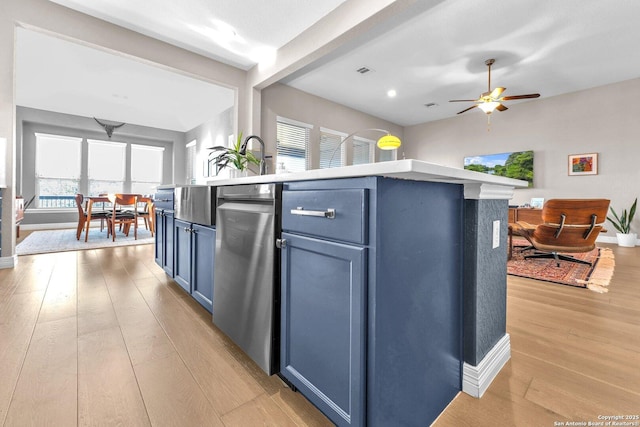 kitchen with blue cabinets, a wealth of natural light, a center island with sink, and light wood-type flooring