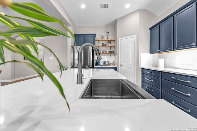 kitchen featuring blue cabinetry, light stone counters, and backsplash