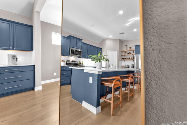 kitchen featuring blue cabinetry, a kitchen bar, a center island, stainless steel appliances, and light hardwood / wood-style floors