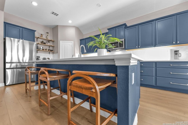 kitchen featuring light hardwood / wood-style flooring, blue cabinetry, stainless steel appliances, a center island, and a kitchen bar