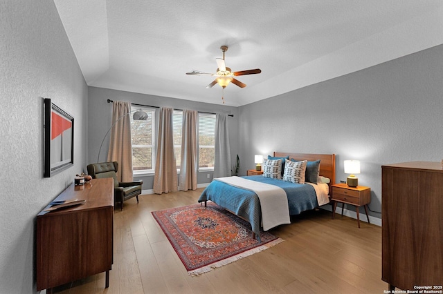 bedroom featuring a raised ceiling, ceiling fan, and light wood-type flooring