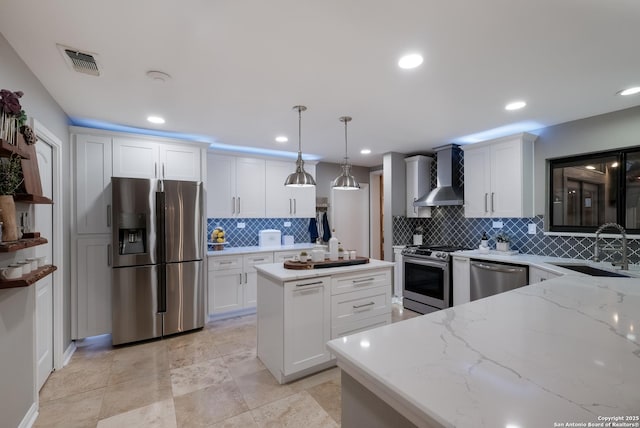 kitchen with white cabinets, appliances with stainless steel finishes, decorative light fixtures, and wall chimney range hood