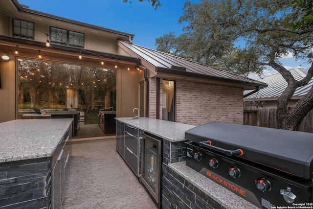 patio terrace at dusk with wine cooler, grilling area, exterior kitchen, and a wet bar