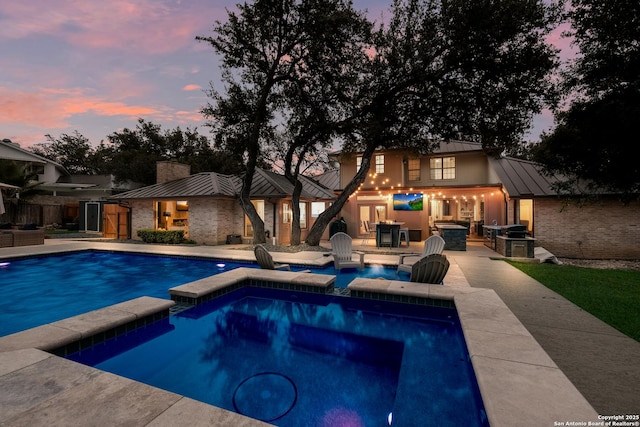 pool at dusk with a grill, a patio area, and an in ground hot tub