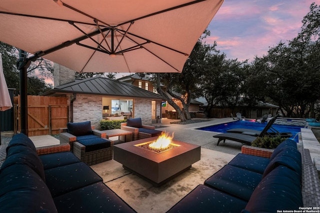 patio terrace at dusk with a fenced in pool and an outdoor living space with a fire pit