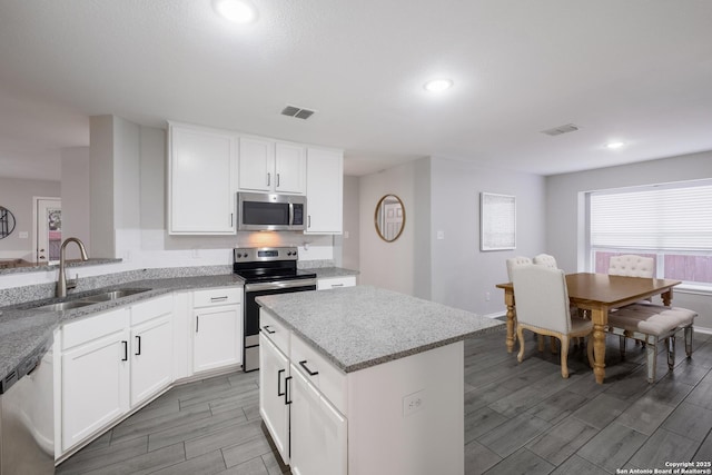 kitchen with appliances with stainless steel finishes, light stone countertops, sink, and white cabinets