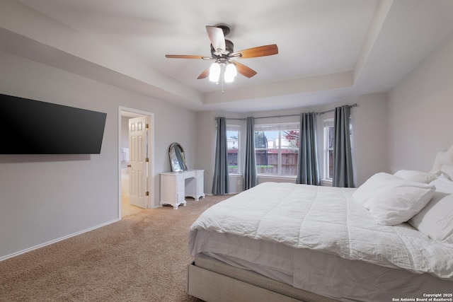 bedroom with a raised ceiling, ceiling fan, light carpet, and ensuite bath