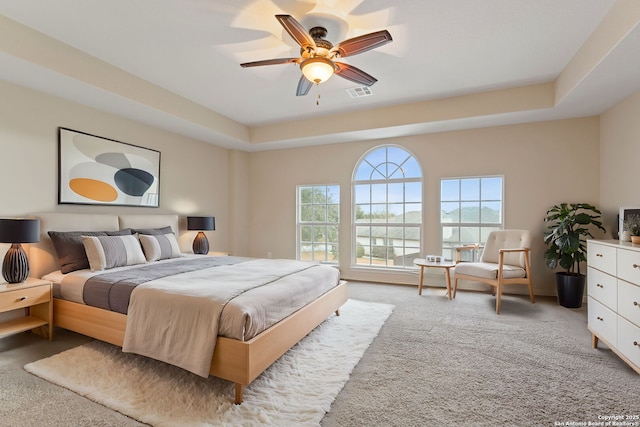 bedroom with light carpet, a tray ceiling, and ceiling fan