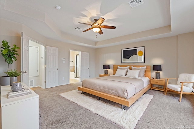 carpeted bedroom featuring ceiling fan, ensuite bath, and a tray ceiling