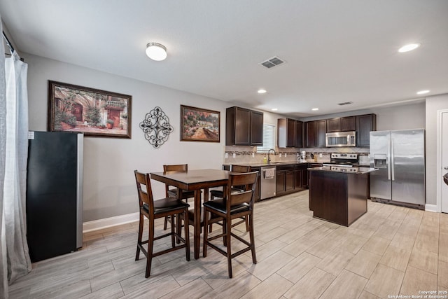 kitchen featuring sink, stainless steel appliances, tasteful backsplash, dark brown cabinetry, and a kitchen island