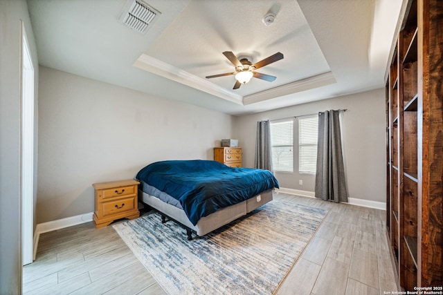 bedroom featuring ceiling fan, a tray ceiling, ornamental molding, a textured ceiling, and light wood-type flooring