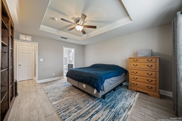 bedroom featuring ensuite bath, ornamental molding, light hardwood / wood-style floors, and a raised ceiling