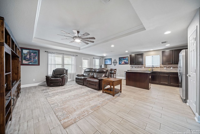 living room featuring sink, crown molding, a raised ceiling, and ceiling fan