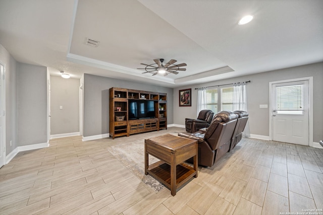 living room featuring a raised ceiling and ceiling fan