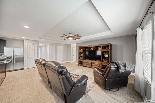 living room featuring ceiling fan, a tray ceiling, and light hardwood / wood-style flooring