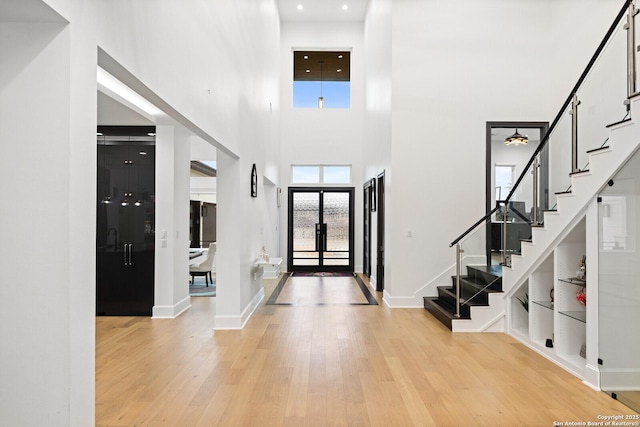 foyer entrance with a towering ceiling and light wood-type flooring