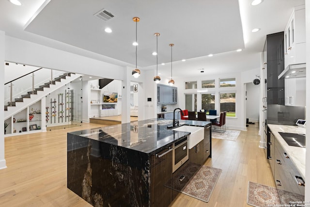 kitchen with sink, dark stone countertops, white cabinets, light wood-type flooring, and a spacious island