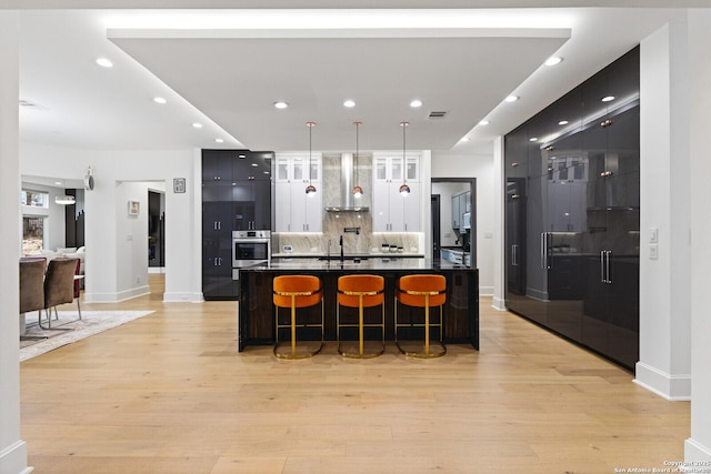 kitchen featuring tasteful backsplash, a breakfast bar area, oven, wall chimney range hood, and light wood-type flooring