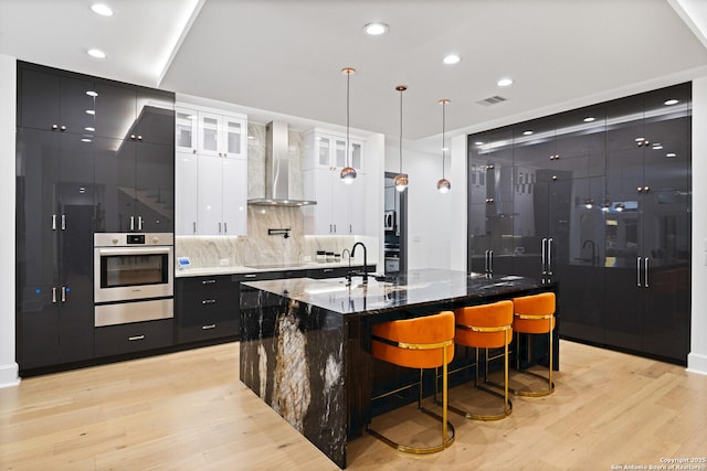 kitchen with white cabinetry, stainless steel oven, wall chimney exhaust hood, and a large island