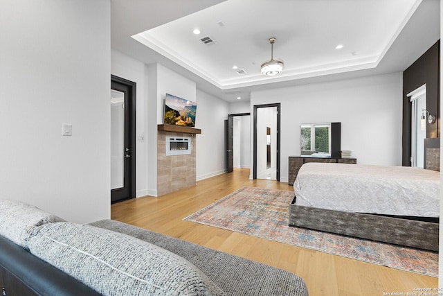 bedroom with a raised ceiling, a tiled fireplace, and light hardwood / wood-style flooring