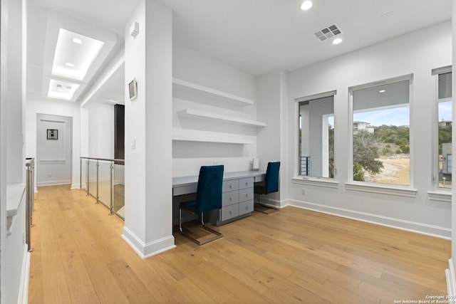 unfurnished office with built in desk, light wood-type flooring, and built in shelves