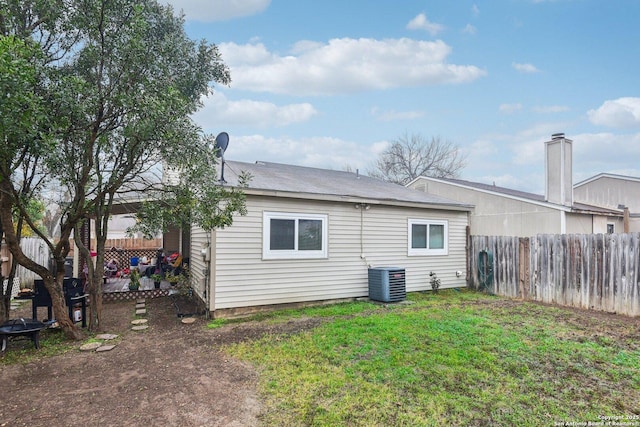 rear view of house with central air condition unit, a fire pit, a yard, and a fenced backyard