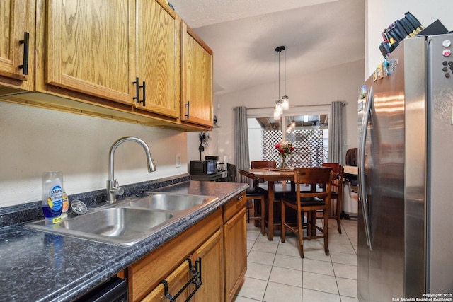 kitchen featuring light tile patterned flooring, freestanding refrigerator, a sink, dark countertops, and decorative light fixtures