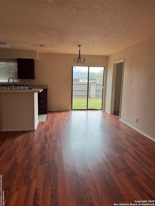 unfurnished living room with dark hardwood / wood-style flooring, a notable chandelier, and a textured ceiling