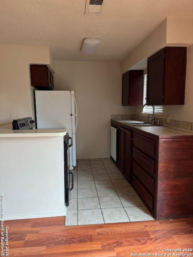 kitchen with white dishwasher, sink, a textured ceiling, and light wood-type flooring