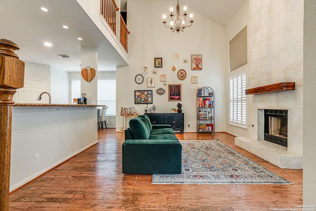 living room featuring a towering ceiling, hardwood / wood-style floors, a fireplace, sink, and an inviting chandelier