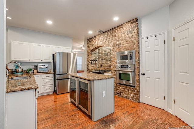 kitchen featuring sink, appliances with stainless steel finishes, dark stone countertops, a center island, and white cabinets