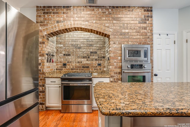 kitchen featuring light stone countertops, stainless steel appliances, light hardwood / wood-style floors, and brick wall