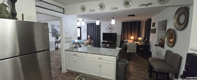 kitchen featuring stone countertops, dark hardwood / wood-style floors, stainless steel refrigerator, white cabinetry, and hanging light fixtures