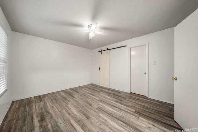 unfurnished bedroom with hardwood / wood-style floors, a barn door, and ceiling fan