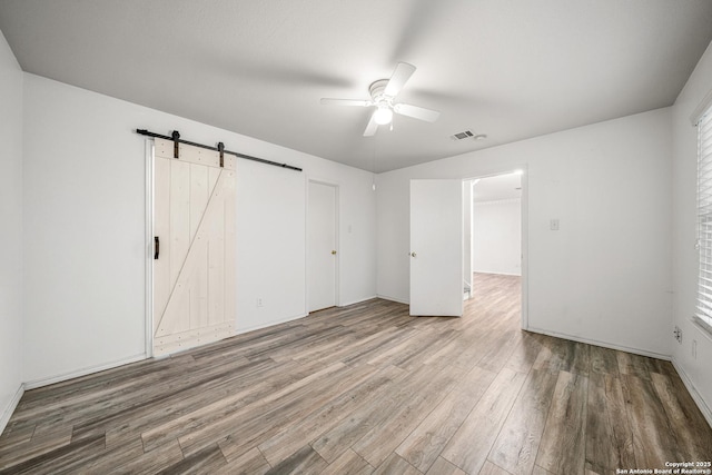 unfurnished bedroom with wood-type flooring, a barn door, and ceiling fan