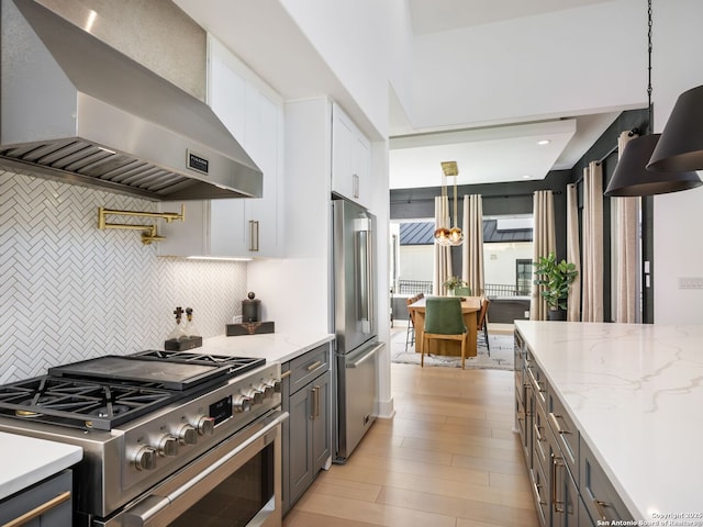 kitchen featuring white cabinetry, light stone counters, high end appliances, hanging light fixtures, and exhaust hood