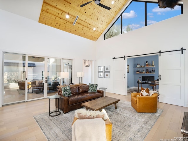 living room with ceiling fan, high vaulted ceiling, wooden ceiling, a barn door, and light wood-type flooring