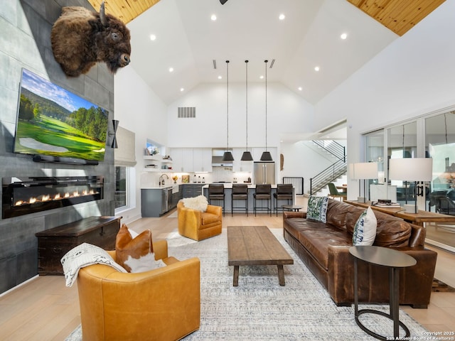 living room with a tiled fireplace, high vaulted ceiling, and light hardwood / wood-style flooring