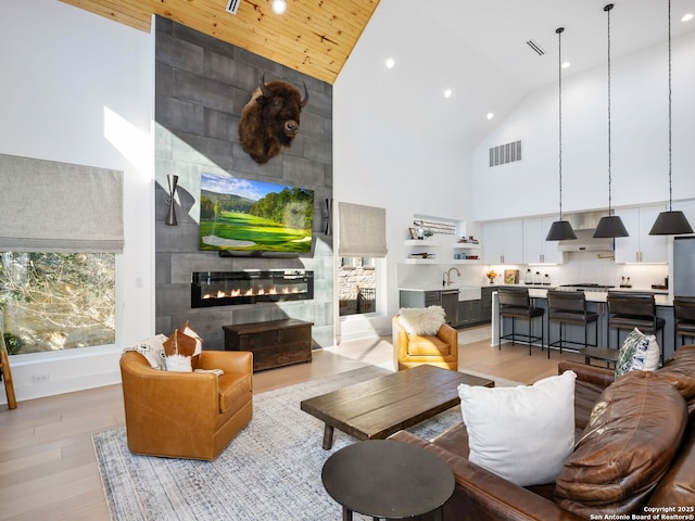 living room featuring light hardwood / wood-style floors, sink, a tiled fireplace, and high vaulted ceiling