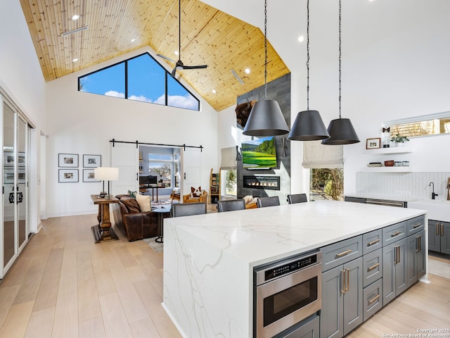 kitchen featuring stainless steel microwave, decorative light fixtures, sink, a barn door, and light stone countertops