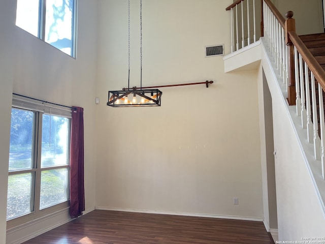 unfurnished dining area featuring a high ceiling, a healthy amount of sunlight, and dark wood-type flooring