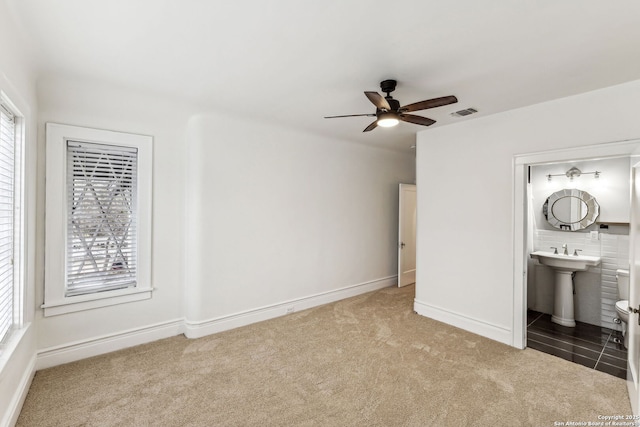 unfurnished bedroom featuring sink, connected bathroom, carpet, and multiple windows