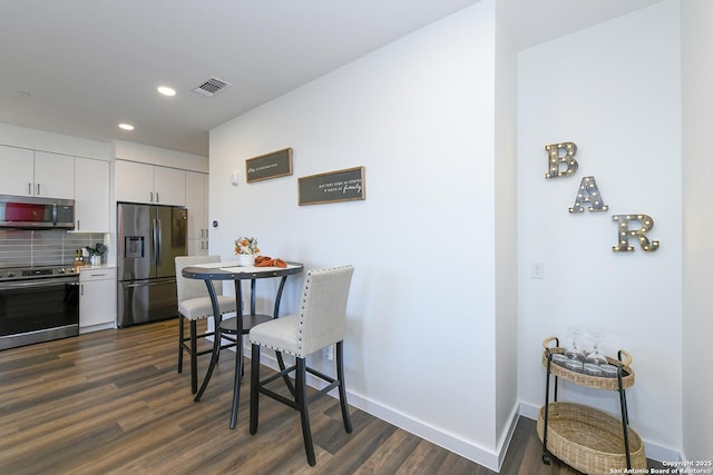 kitchen with white cabinetry, appliances with stainless steel finishes, backsplash, and dark hardwood / wood-style flooring