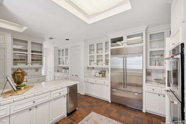 kitchen featuring appliances with stainless steel finishes, white cabinetry, decorative backsplash, tile counters, and crown molding